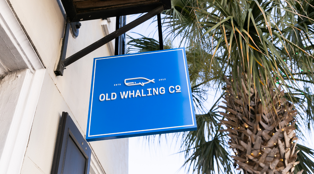 Blue and white logo sign for Old Whaling Company outside King Street shop with palm tree in background