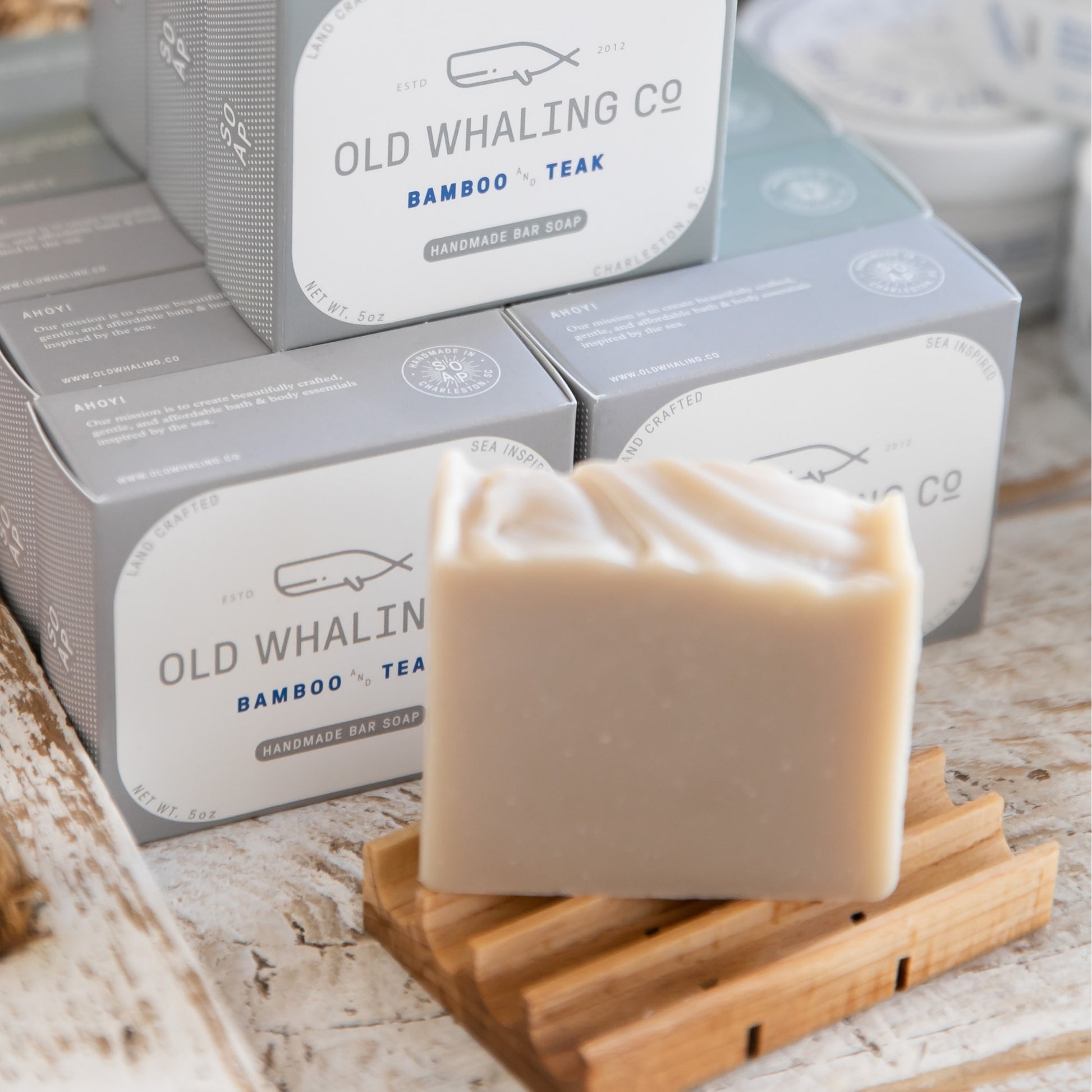 Bamboo & Teak Bar Soap sitting on wood soap dish in front of Bamboo & Teak Soap display