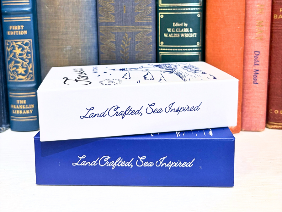 Match Box with 'Land Crafted, Sea Inspired' text on a background of books