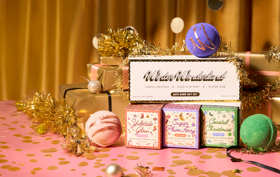 Bath bomb gift set with decorative packaging on a pink surface with gold tinsel.