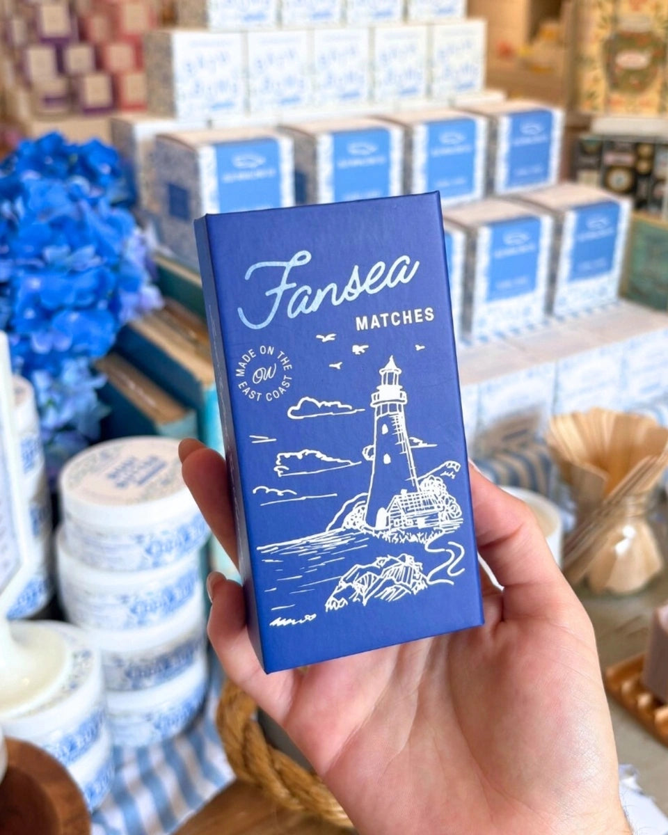 Blue matches box with lighthouse design held by a hand, with more boxes in the background.