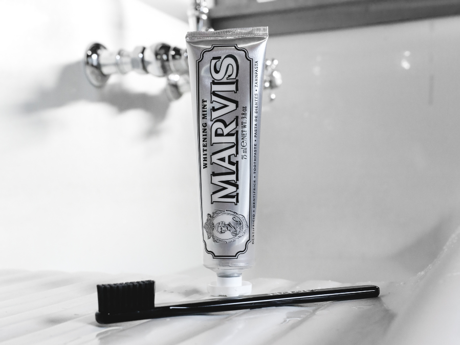 Marvis toothpaste tube with a black toothbrush on a white bathroom sink