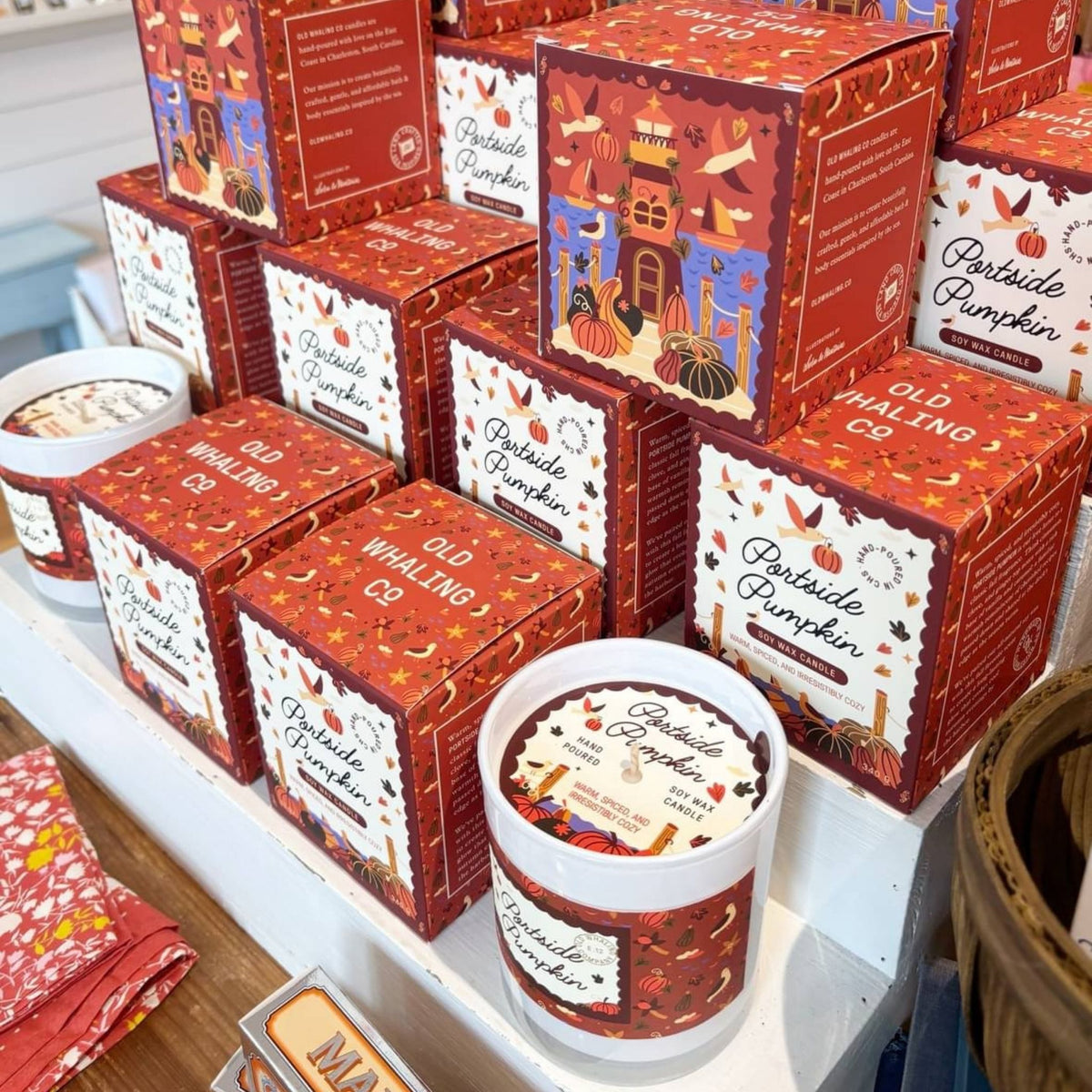 A retail display of Portside Pumpkin Candles, showing multiple red and white illustrated boxes arranged on white shelves.