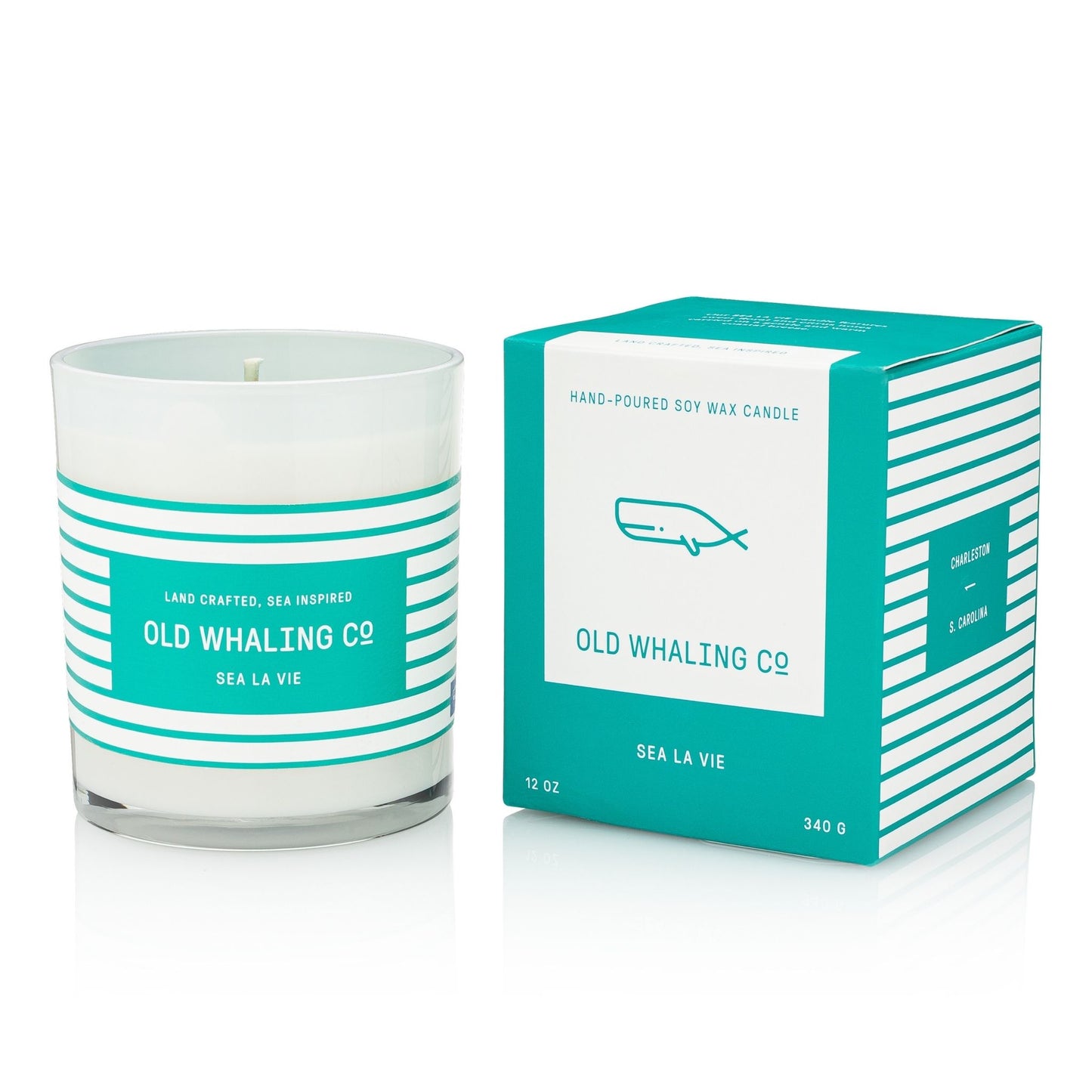 A white soy wax candle in a clear glass jar with teal and white horizontal stripes, shown next to its matching square box. The packaging features a white center panel with a teal whale illustration and the text 'OLD WHALING CO' and 'SEA LA VIE'.