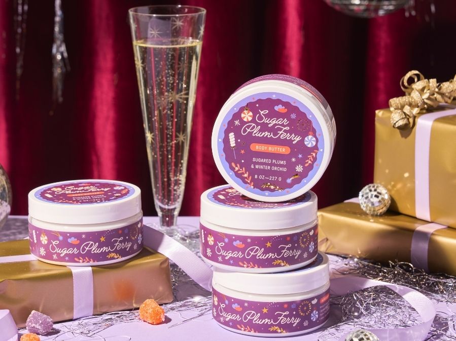 Body butter jars of 'Sugar Plum Fairy' with a glass of champagne and gift boxes on a festive background