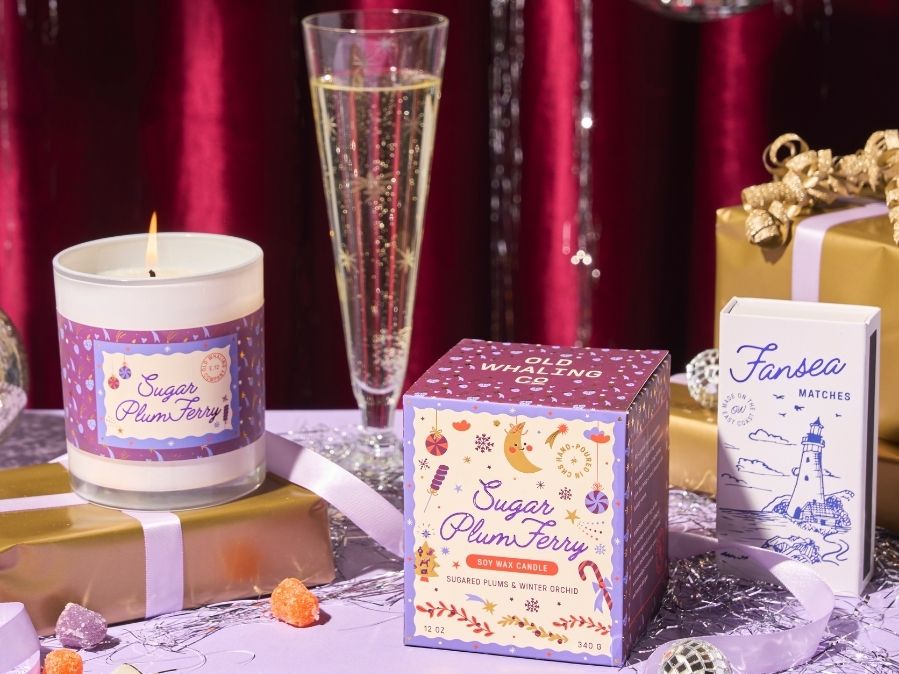 Candle, champagne flute, and gift boxes with festive labels on a red background