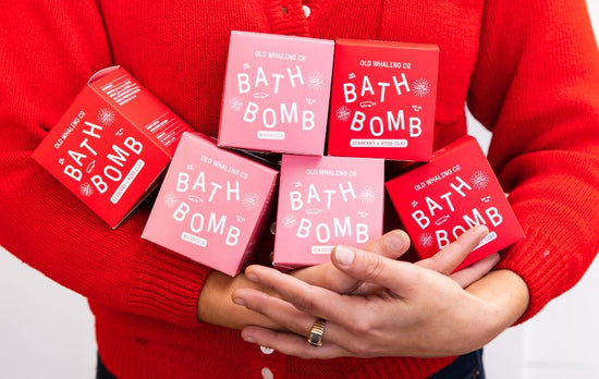 Employee in red sweater holding red and pink Magnolia and Seaberry bath bomb boxes