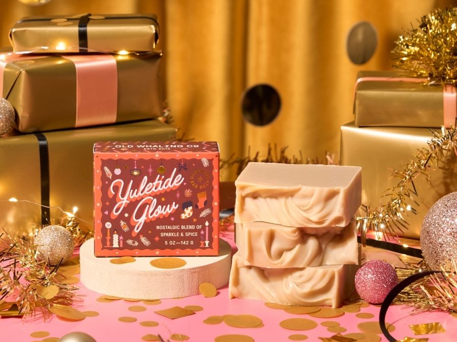 Yuletide Glow soap bar with decorative packaging on a festive background with gold presents and Christmas decorations.