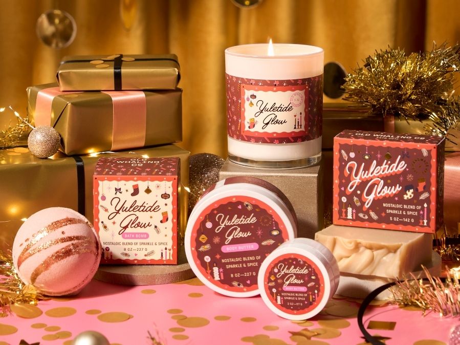 Yulethide Glow bath and body collection next to gift boxes on a decorative surface with festive decorations.
