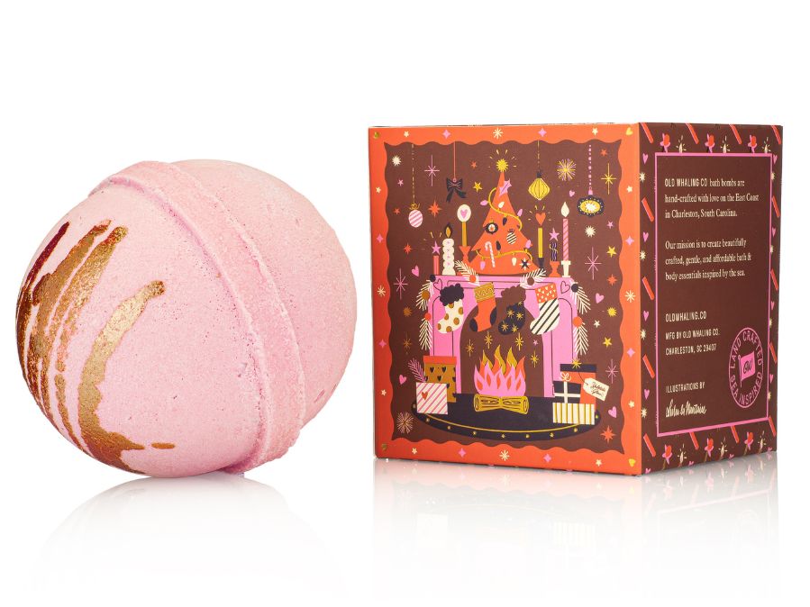 Pink bath bomb with gold drizzle next to its decorative box on a white background