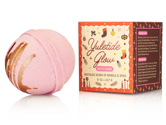 Pink bath bomb with gold swirls next to its packaging on a white background